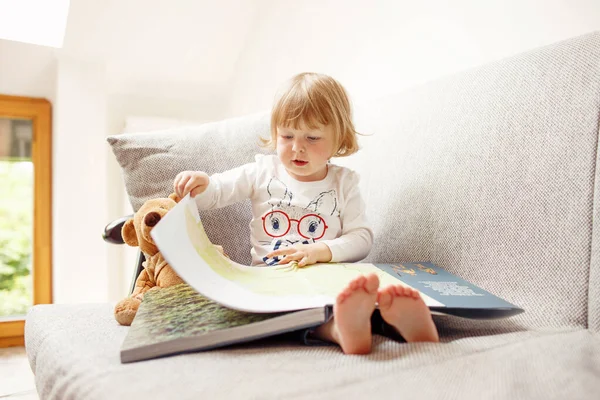 Child turning pages of big book while seating on a sofa