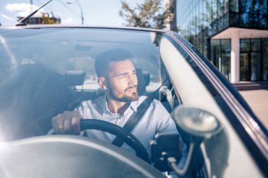 Genç adam ofisin yakınına park ediyor. İşadamı birinci sınıf otomatikte kareli gömlek giyiyor.