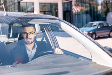 Ofisin yanındaki arabada oturan kareli gömlek ve ceket giyen başarılı genç adam.