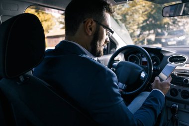 Genç sakallı adam arabada otururken e-posta yazıyor.