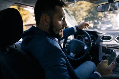 Telefonu elinde, arabada oturan üzgün genç bir adam.