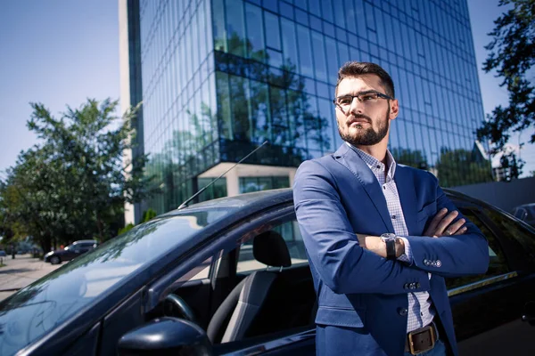 Kararlı iş adamı arabanın yanında duruyor. Arka plandaki ofis binası.