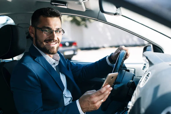 Arabada elinde telefon tutan gülümseyen genç adam.