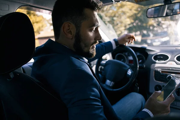 Telefonu elinde, arabada oturan üzgün genç bir adam.