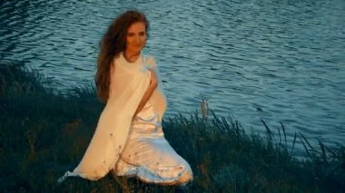 Nehir kıyısında beyaz bir elbise içinde oturan kadın