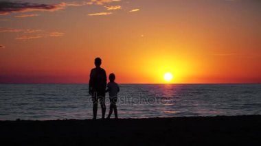 Anne ve çocuk siluetleri ve günbatımı denize