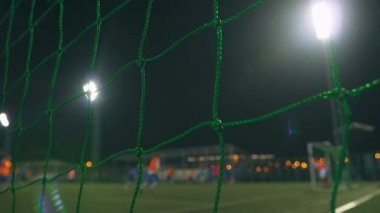 Akşam futbol maçı. Antrenman sahasında oynayan futbolcular, stadyum ışıklarıyla aydınlatılıyor. Hedef ağıyla görüntüle.