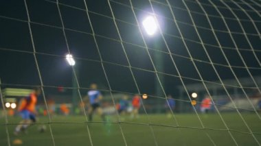 Akşam futbol maçı. Antrenman sahasında oynayan futbolcular, stadyum ışıklarıyla aydınlatılıyor. Hedef ağıyla görüntüle.