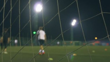 Akşam futbol maçı. Antrenman sahasında oynayan futbolcular, stadyum ışıklarıyla aydınlatılıyor. Hedef ağıyla görüntüle.