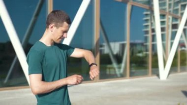 Güneşli bir günde modern bir binanın yakınındaki bisiklet yolunda bisiklet süren genç bir adam, stedicam görüntüsü.