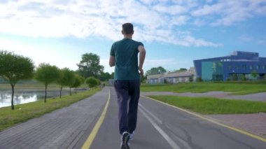 Genç sporcu sabahın köründe koşuyor. Şehir parkındaki pitoresk nehir boyunca koşar. Buharlı çekim.