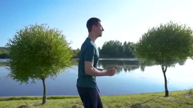 Genç sporcu sabahın köründe koşuyor. Şehir parkındaki pitoresk nehir boyunca koşar. Buharlı çekim.