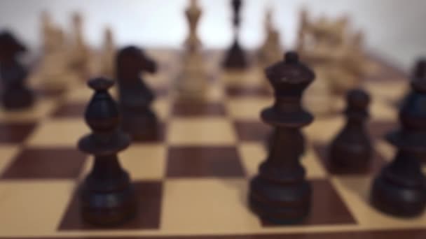 Échecs en bois noir et blanc sur l'échiquier dans des positions de départ prêtes pour le jeu. Un fond blanc. Gros plan. Mouvement horyzontal de la caméra, prise de vue de poupée .