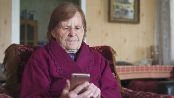 一位老年妇女拿着手机进行视频通话 她看着手机屏幕 微笑着挥挥手 — 图库视频影像