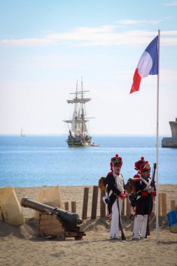 Malaga, İspanya - 26 Ekim 2014: Büyük Ordu 'nun Napolyon askerleri kıyıda dalgalanan bir Fransız bayrağı ve bir topun yanında. Bir gemi yelken açıyor. 1812 'deki İngiliz çıkartmasının tarihi canlandırması..