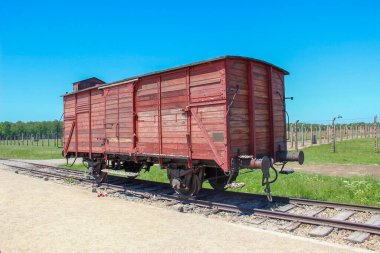 Oswiecim, Polonya - 20 Mayıs 2012: Auschwitz-Birkenau toplama kampının demiryolu girişinde arkasında elektrikli dikenli tellerle terk edilmiş tren vagonu. Mavi gökyüzüyle güneşli bir gün.