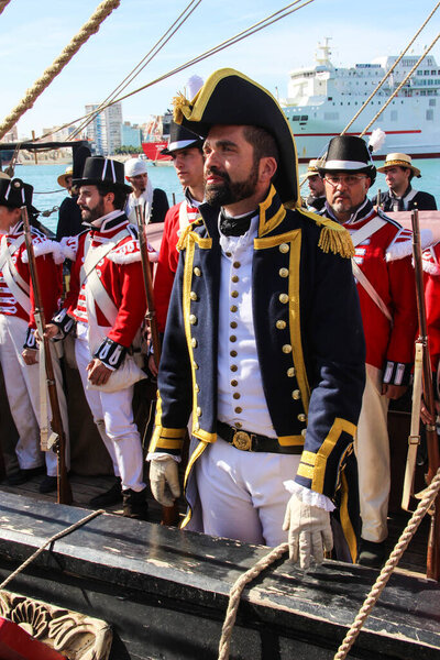 Malaga, Spain - October 26, 2014: Captain of the 18th century Royal Navy on a ship with his crew. People behind with the royal marines uniform, red coat and black felt round hat. Reenactors.