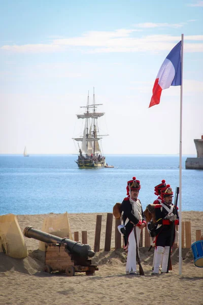 Malaga, İspanya - 26 Ekim 2014: Büyük Ordu 'nun Napolyon askerleri kıyıda dalgalanan bir Fransız bayrağı ve bir topun yanında. Bir gemi yelken açıyor. 1812 'deki İngiliz çıkartmasının tarihi canlandırması..