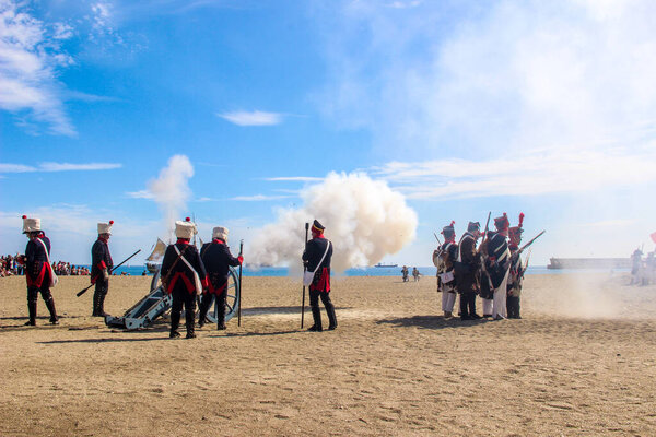 Malaga, Spain - October 26, 2014: 18th century french soldiers firing a cannon with gunpowder. Men and women reenactors. Historical reenactment of a Napoleonic corsair base.