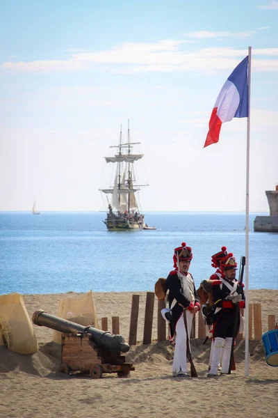 2014年10月26日 西班牙马拉加 伟大军队的拿破仑士兵坐在一面飘扬的法国国旗和海滩上的大炮旁边 一帆风顺地离开了 1812年英国登陆的历史重演 图库图片