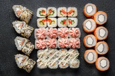 Karanlık bir arka planda geleneksel Japon yemekleri. Suşi, nigiri, çiğ somon bifteği, pilav, krem peynir, avokado, limon, zencefil turşusu. Asya yemekleri. Akşam yemeği partisi.