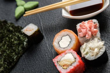 Karanlık bir arka planda geleneksel Japon yemekleri. Suşi, nigiri, çiğ somon bifteği, pilav, krem peynir, avokado, limon, zencefil turşusu. Asya yemekleri. Akşam yemeği partisi.