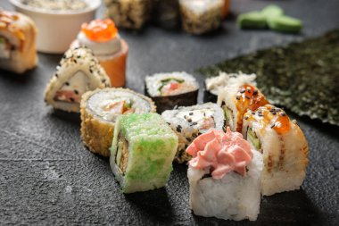 Karanlık bir arka planda geleneksel Japon yemekleri. Suşi, nigiri, çiğ somon bifteği, pilav, krem peynir, avokado, limon, zencefil turşusu. Asya yemekleri. Akşam yemeği partisi.