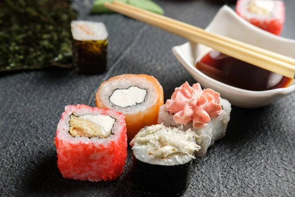 Karanlık bir arka planda geleneksel Japon yemekleri. Suşi, nigiri, çiğ somon bifteği, pilav, krem peynir, avokado, limon, zencefil turşusu. Asya yemekleri. Akşam yemeği partisi.