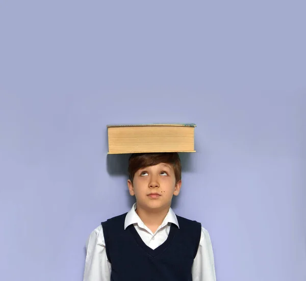 Çocuk kafasında büyük bir kitap tutuyor ve ona bakıyor. Eğitim kavramı.