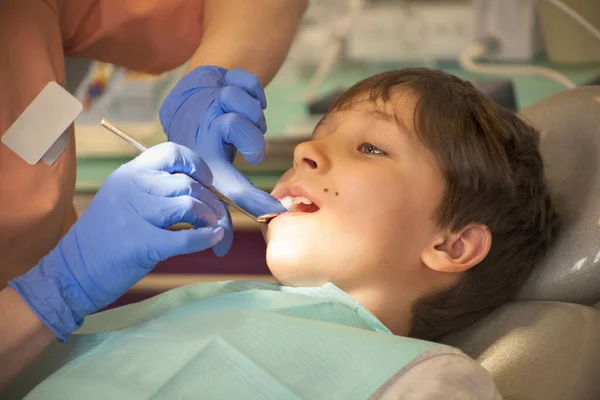Mavi eldivenli dişçi klinikteki aynayla çocuğun dişlerine bakıyor..