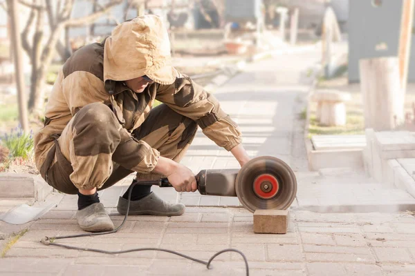 İşçi açık havada dairesel kesiciyle asfalt kesiyor.