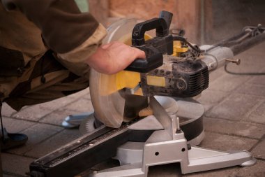 Üniformalı marangoz dairesel testereyle çalışıyor, küçük tahta etek tahtalarını kesiyor. Talaşlar düşüyor..