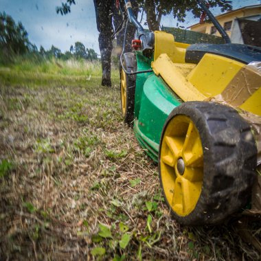 Hareket eden sarı ve yeşil bir çim biçme makinesinin yakın ve açılı görüntüsü