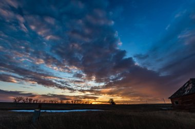 Tarlanın üzerinde güneş batıyor ve terk edilmiş evler. Gliechen, Alberta, Kanada