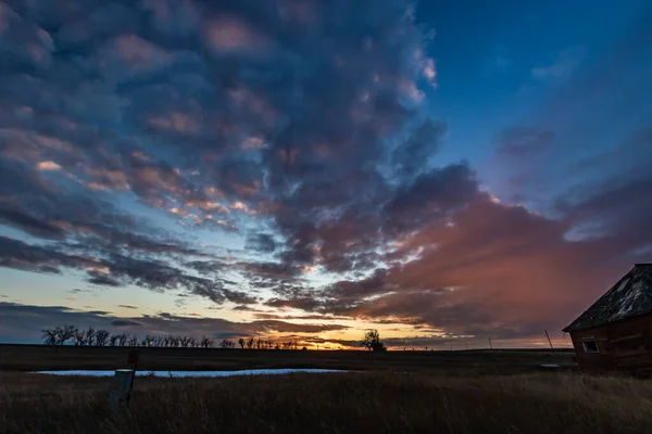 Tarlanın üzerinde güneş batıyor ve terk edilmiş evler. Gliechen, Alberta, Kanada