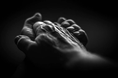 Siyah ve beyaz. Kırışık eller siyah bir arka planda bir araya toplanmış.