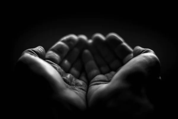 Black and white. Wrinkled hands with folded palms on a black background