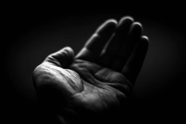 Black and white. Wrinkled left hand asks for help on a black background