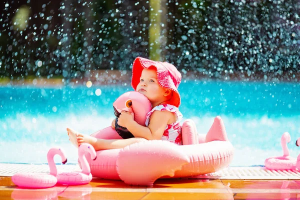 Toddler girl in pink Panama hat hugging pink rubber flamingo swimming ring Royalty Free Stock Photos