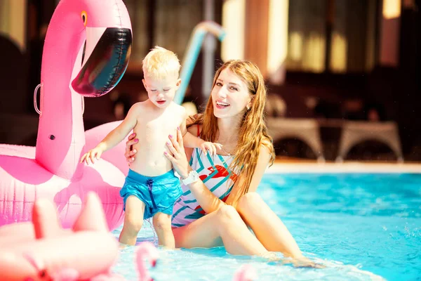 Pretty mother hugging her little blond son in the pool with flamingo swim ring Stock Image