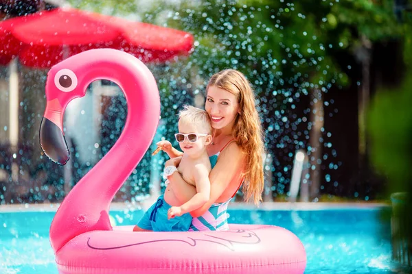 Pretty mother hugging her little blond son in the pool with flamingo swim ring Stock Image