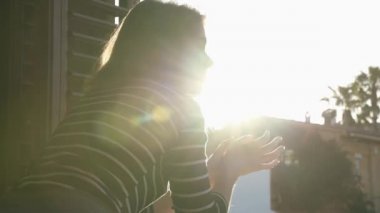 Odasının penceresinde alkışlayan bir kız, kovid-19 için sağlık hizmetlerine teşekkür ediyor. Arkaplanda gün batımı.
