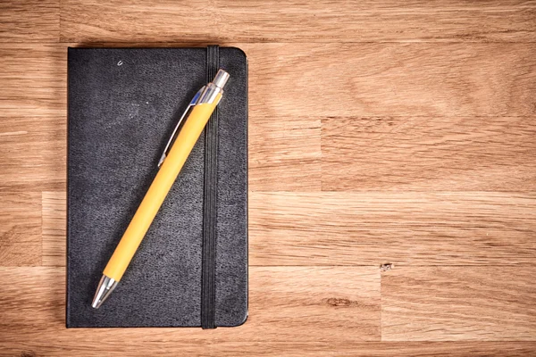 Closed notebook and ballpoint on a brown wooden table — Stock Photo, Image