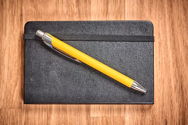 Closed notebook and ballpoint on a brown wooden table — Stock Photo, Image