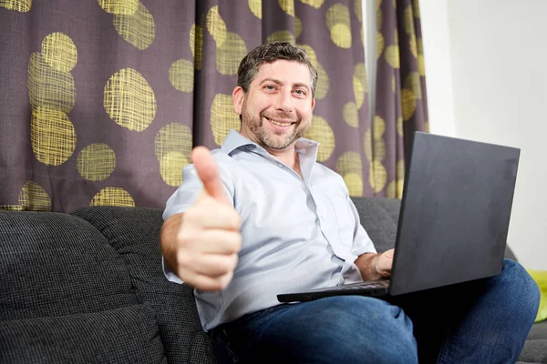 Thumbs up man with laptop on sofa