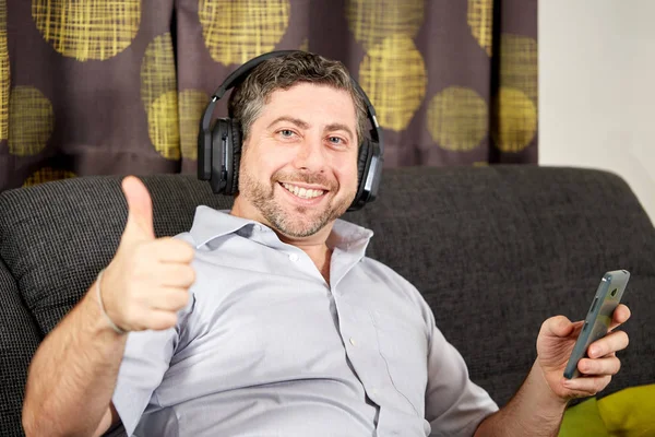 Man thumbs up with headphones on sofa