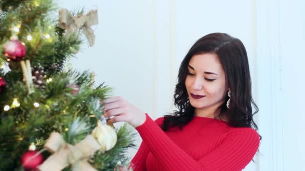 Όμορφο κορίτσι στολίζει ένα χριστουγεννιάτικο δέντρο τα Χριστούγεννα. Να χαμογελά όμορφα. Είναι πολύ όμορφο και ελκυστικό. Νέο έτος 2017. — Αρχείο Βίντεο