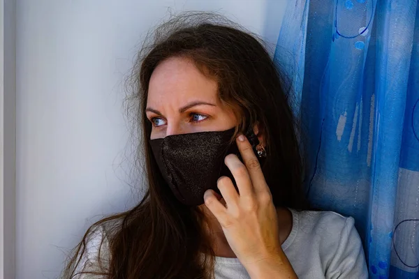 Pencerenin yanındaki pencerenin pervazında koruyucu maskeli bir kız. Gizli virüs salgınına karşı korunma amaçlı. Tedavi, Önleme, Tecrit