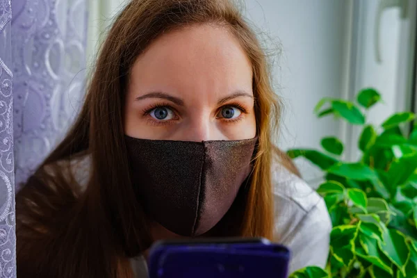 Pencerenin yanındaki pencerenin pervazında koruyucu maskeli bir kız. Gizli virüs salgınına karşı korunma amaçlı. Tedavi, Önleme, Tecrit