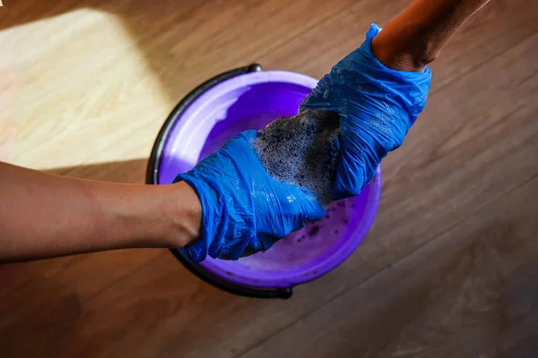 Bir kova su ve çamaşır suyu, virüs dezenfeksiyonu. Eldivenli eller paçavrayı sıkıyor. Kovid-19 'a karşı savaş, tecrit, karantina. Temizlik sağlığın teminatıdır.